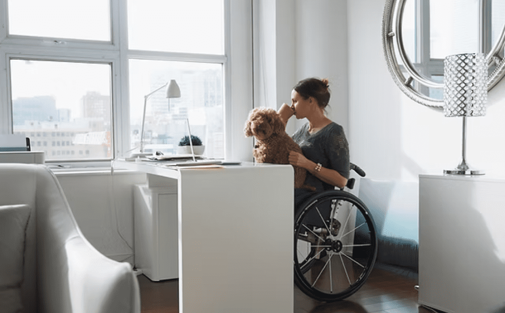 Woman in wheelchair with dog on lap drinking coffee, illustrating NDIS Property Solutions