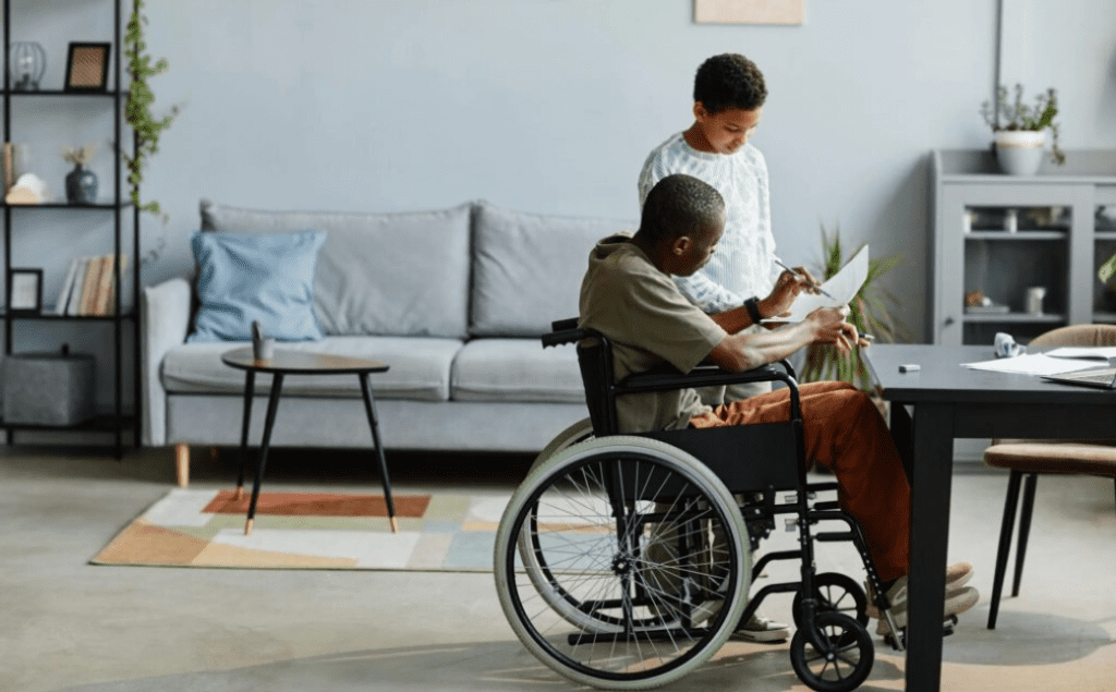Man in wheelchair and boy reviewing documents together at home, illustrating Supported Independent Living